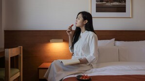 Una persona sentada en una cama con un libro y un plato de rebanadas de sandía.