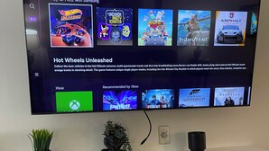 Un téléviseur à écran plat fixé au mur affiche l’interface d’un jeu vidéo, avec différentes options de jeu et une description du jeu « Hot Wheels Unleashed ».
