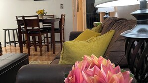 Un salon avec un canapé, une table basse et une lampe. Au fond, on aperçoit une table à manger entourée de chaises.