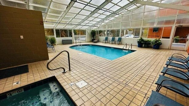 Une piscine intérieure dotée d’un sol carrelé, d’un plafond en verre et de chaises longues disposées autour de la piscine.
