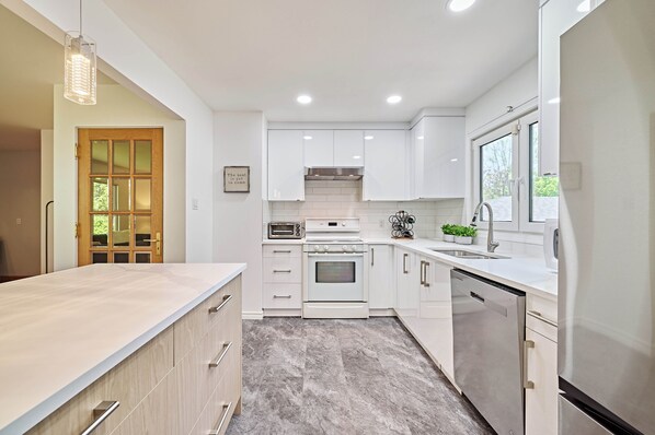 A modern kitchen with white cabinets, a built-in oven, a dishwasher, and a large window.