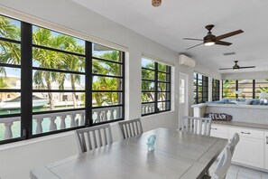 A spacious dining area with a large table and chairs, large windows with a view of palm trees and a pool, and ceiling fans. - Island Paradise-large 2 bedroom/2 bath SFH  with Cabana club and 75ft of dockage (Key Colony Beach)