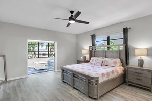 A bedroom with a bed, bedside tables, a ceiling fan, a window with curtains, and a view of greenery outside. - Island Paradise-large 2 bedroom/2 bath SFH  with Cabana club and 75ft of dockage (Key Colony Beach)