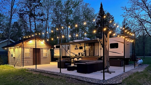 Ein Wohnmobil mit überdachter Terrasse, einer kleinen Hütte und Lichterketten.