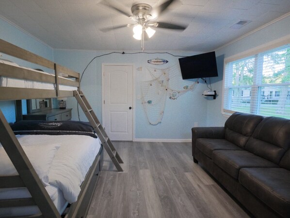 A bedroom with bunk beds, a ceiling fan, a TV mounted on the wall, and a window with blinds.