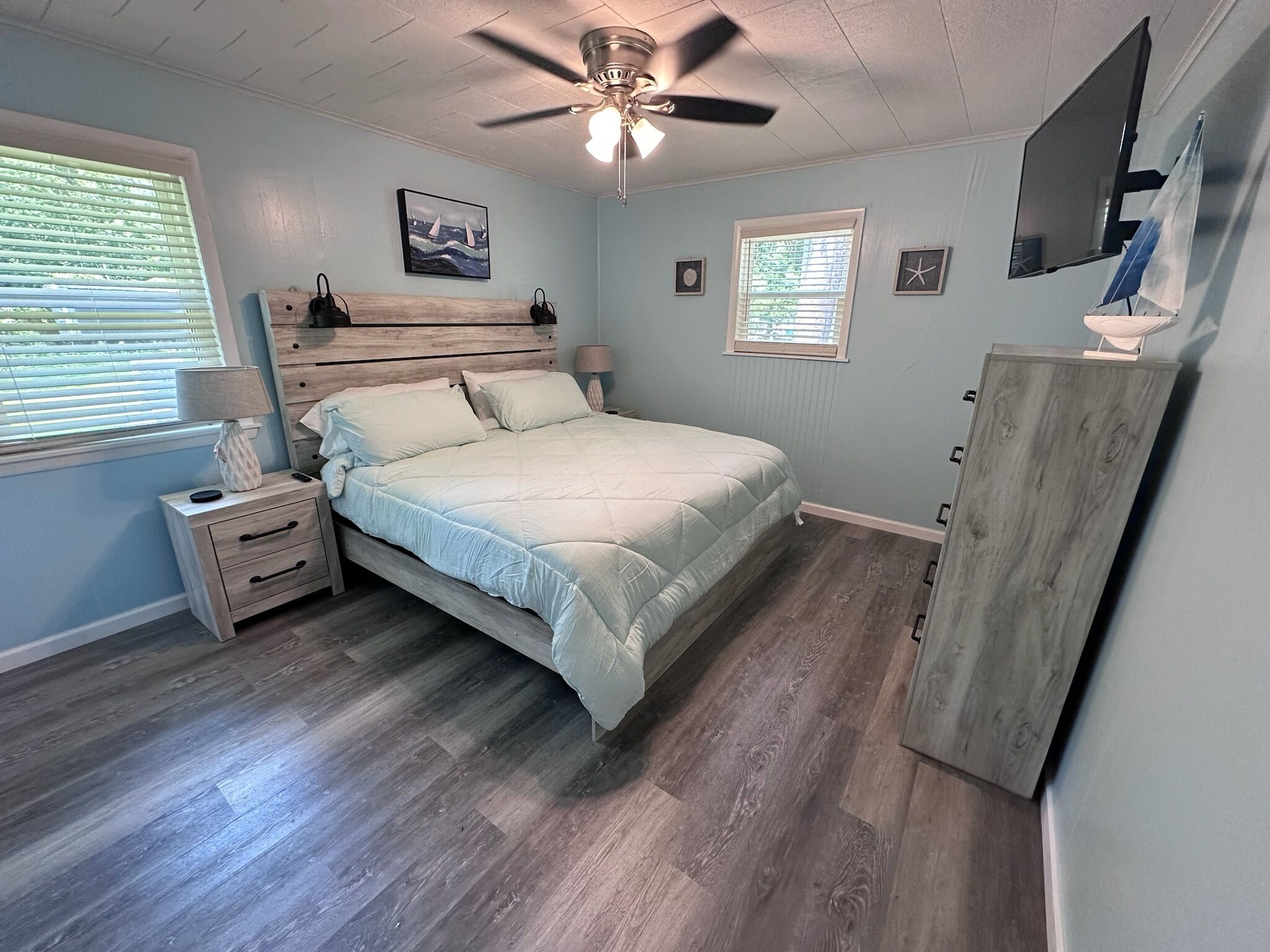 A bedroom with a bed, nightstands, a ceiling fan, a TV, and a wooden cabinet.