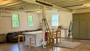 A spacious room with a high ceiling, wooden beams, and large windows. There is a couch, a table, and a ladder leaning against the wall.