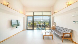 A modern living room with a flat-screen TV, a sofa, a coffee table, and a balcony with a view of the mountains. - Theprism Pension (Goseong)