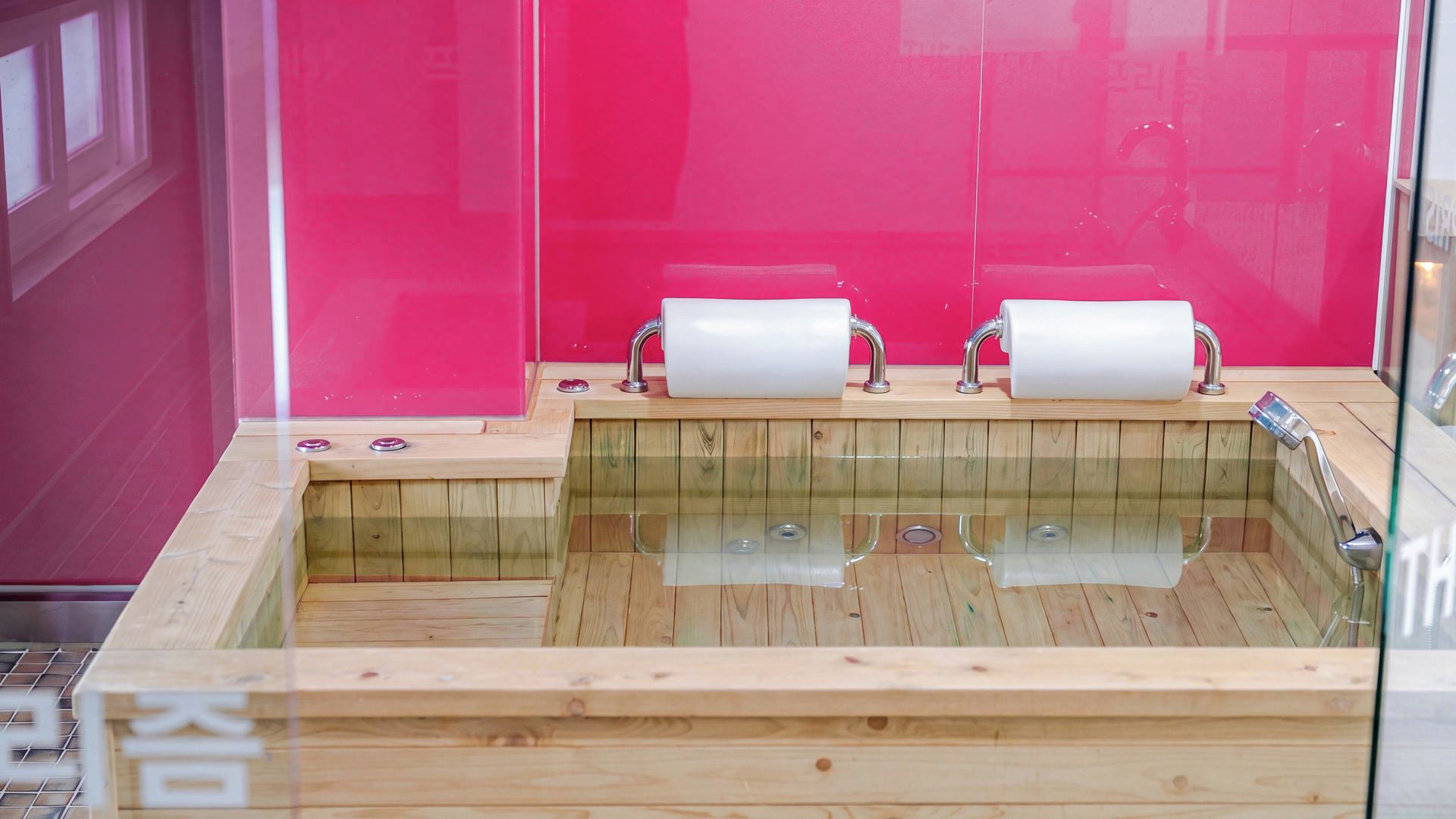 A wooden bathtub with two rolls of toilet paper, a glass enclosure, and a wooden floor.