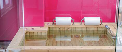 A wooden bathtub with two rolls of toilet paper, a glass enclosure, and a wooden floor.