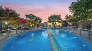 Une piscine entourée d’une terrasse, de rampes et d’arbres.