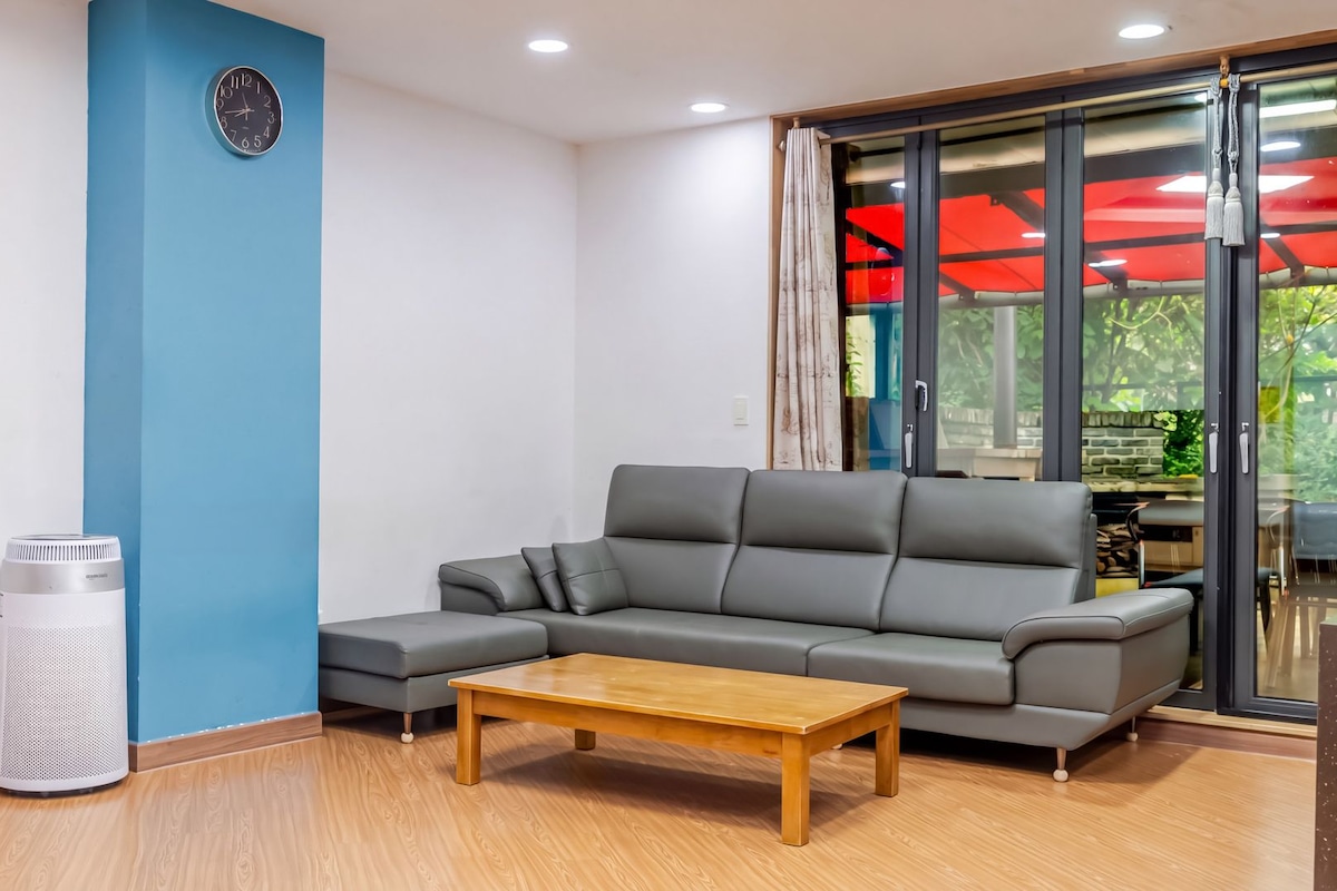 Un salon moderne avec un canapé d’angle gris, une table basse en bois, un haut-parleur blanc et un mur d’accent bleu.