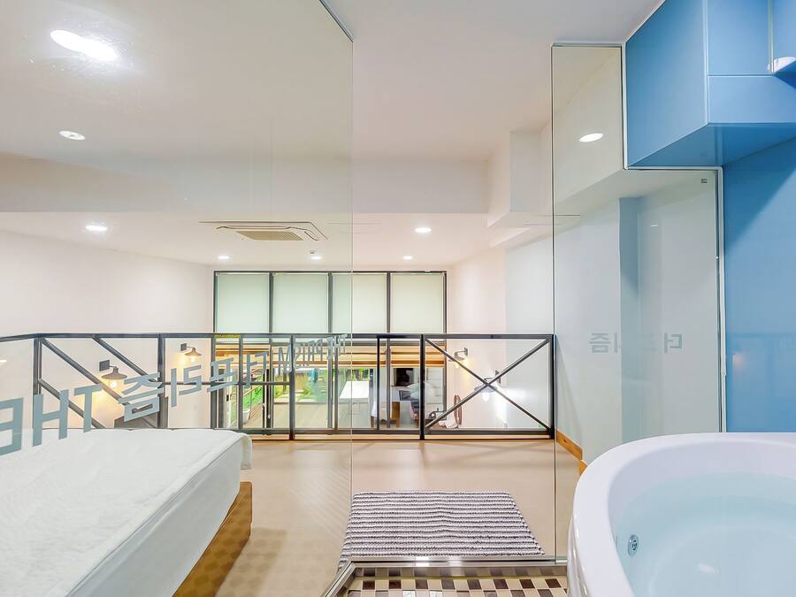 A modern hotel room with a large bathtub, a glass-enclosed balcony, and a staircase leading to an outdoor area.