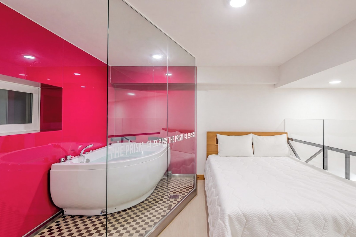 Une chambre à coucher moderne avec un grand lit, une salle de bain fermée par des parois de verre et un sol à carreaux.