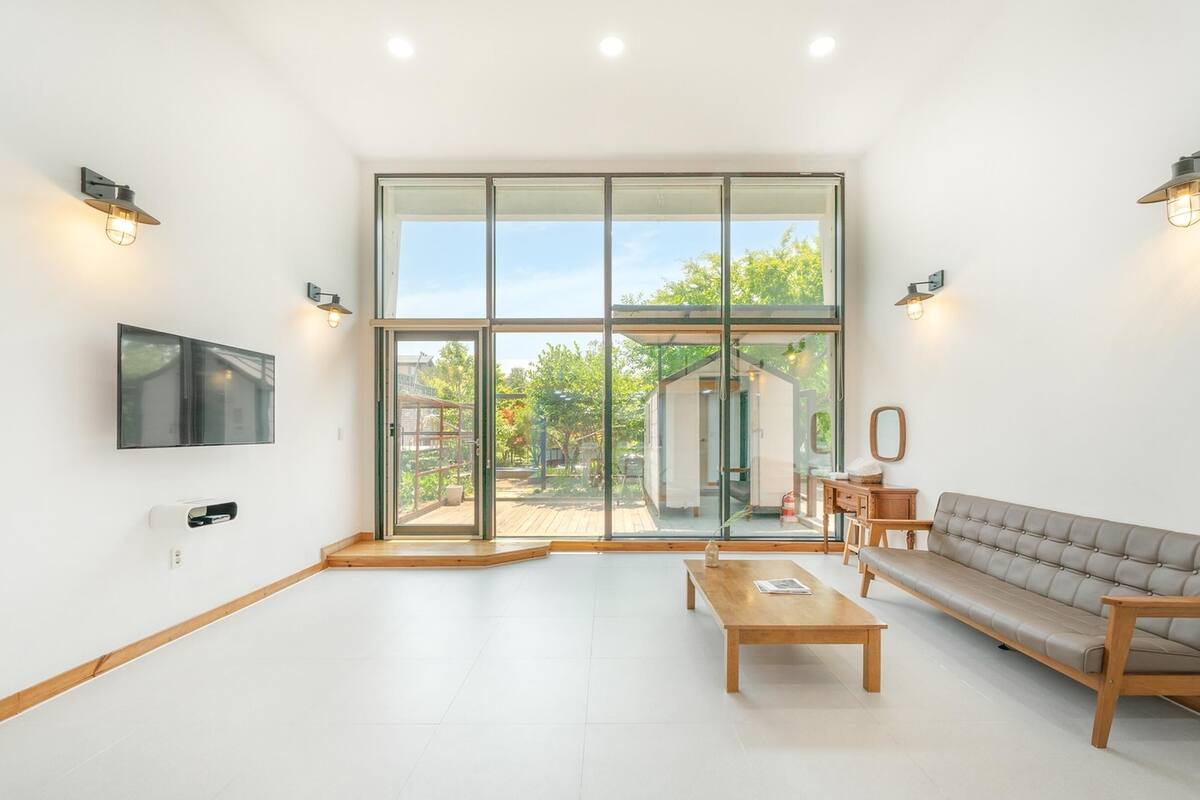 Ein geräumiges Wohnzimmer mit einer großen Glasschiebetür, die zu einem Außenbereich führt, einem wandmontierten Flachbildfernseher, einem Holztisch und einem beigefarbenen Sofa.