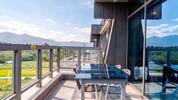 Una terraza moderna al aire libre con una mesa y sillas de vidrio, con vistas a un paisaje montañoso.