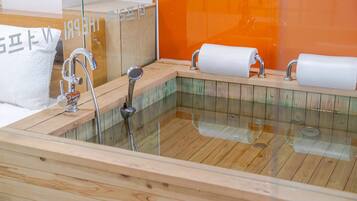 A wooden bathtub with two faucets and a glass enclosure.