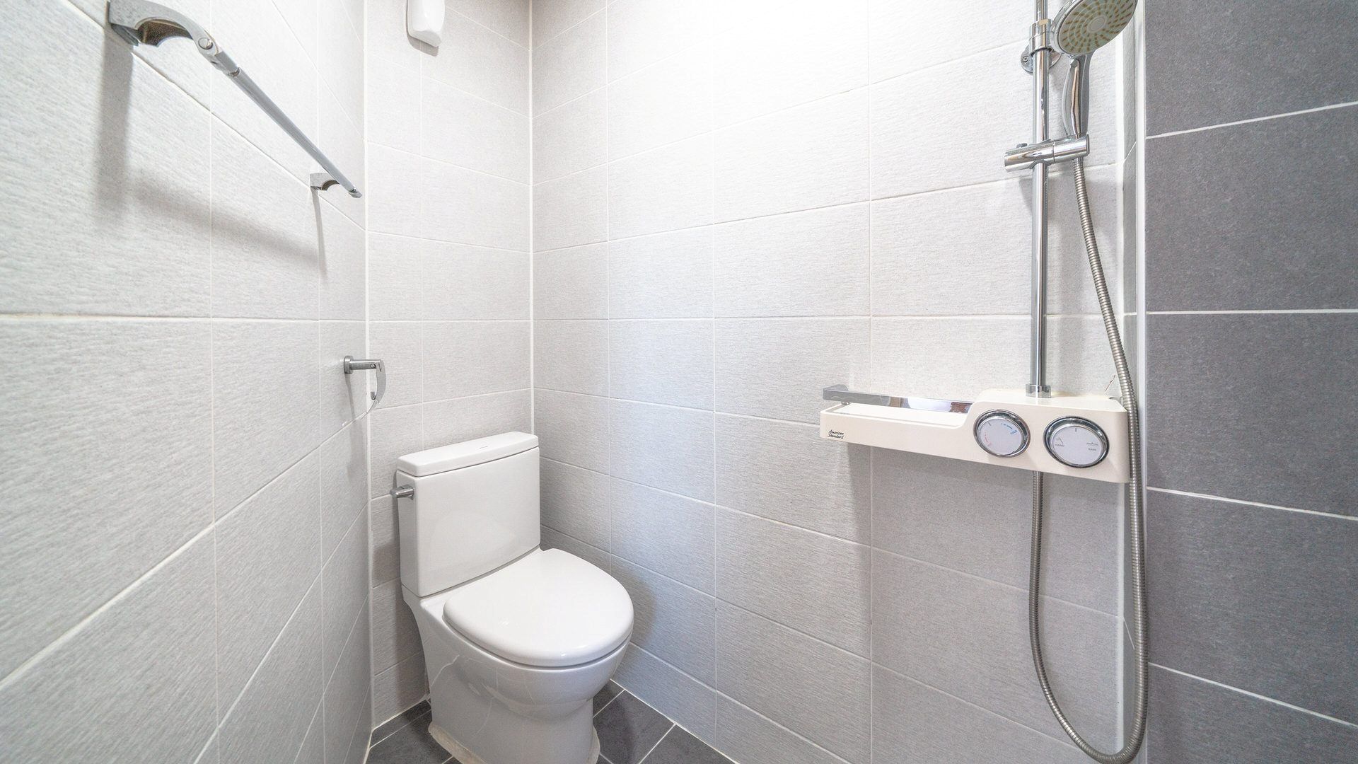 Un baño pequeño y moderno con inodoro, ducha con cabezal de ducha manual y panel de control en la pared.