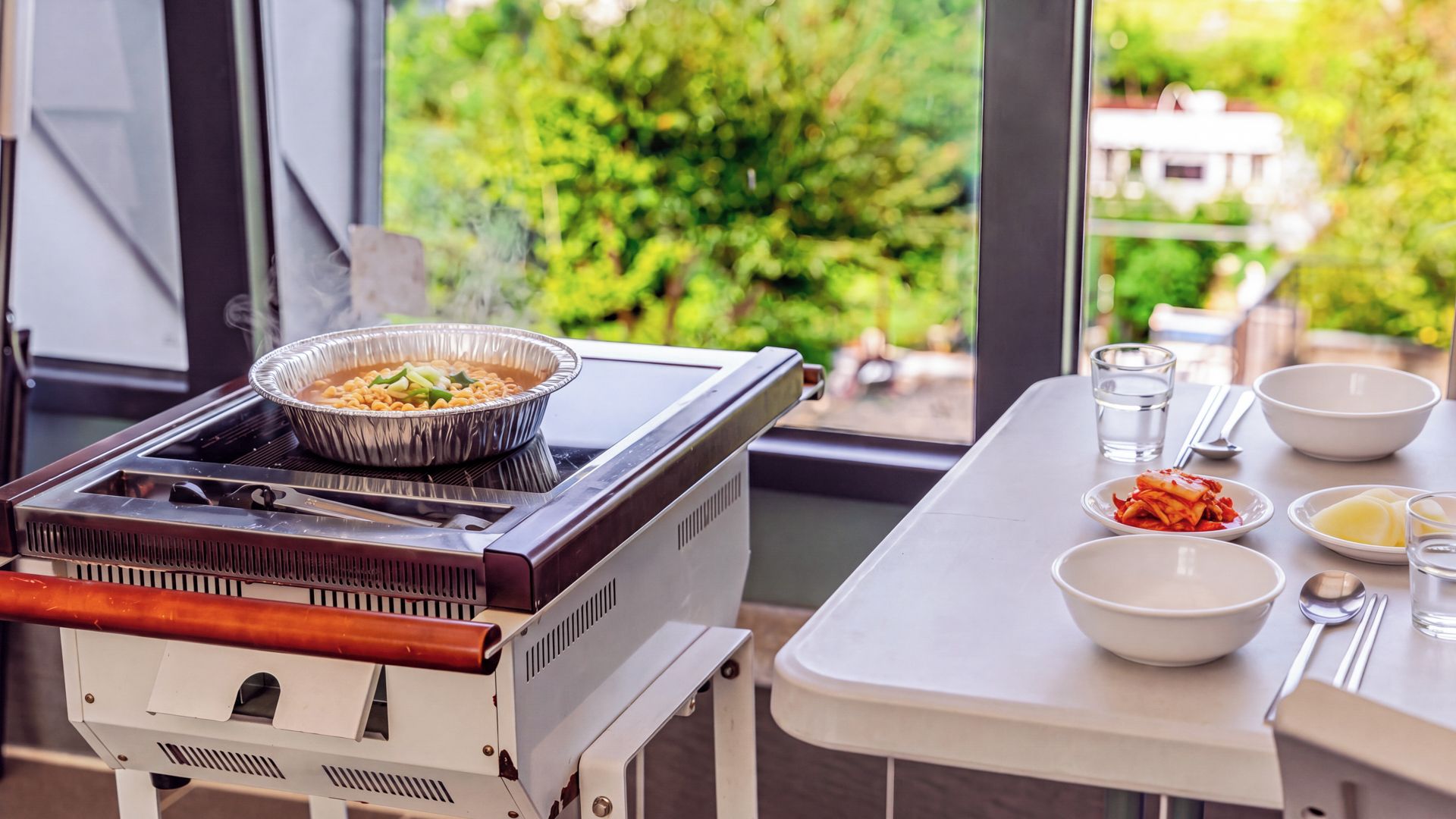 Uma cozinha compacta com fogão, uma tigela de comida e uma mesa de jantar com tigelas e utensílios.