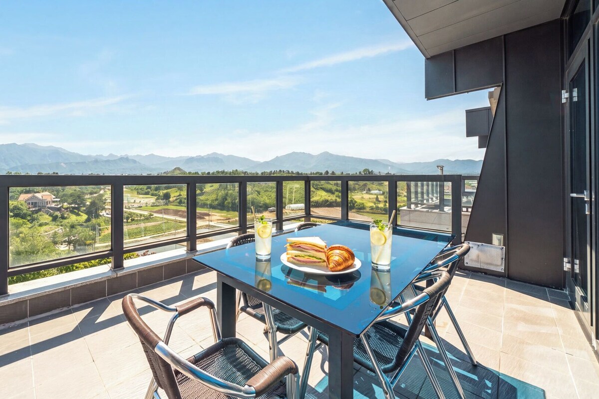 Un balcon avec une table dressée pour deux personnes, offrant une vue sur un paysage montagneux.