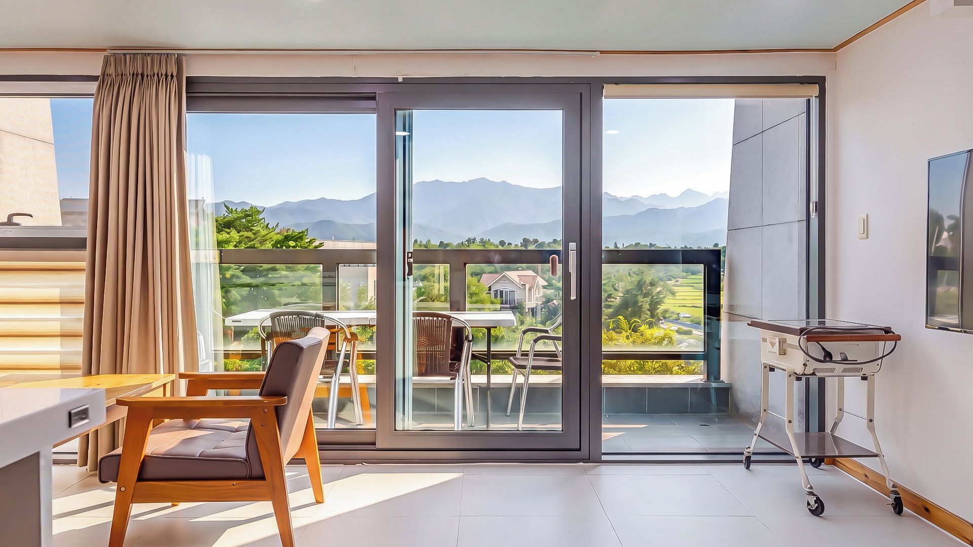 Una habitación moderna con un ventanal corredero que da a un balcón con vistas a la montaña.