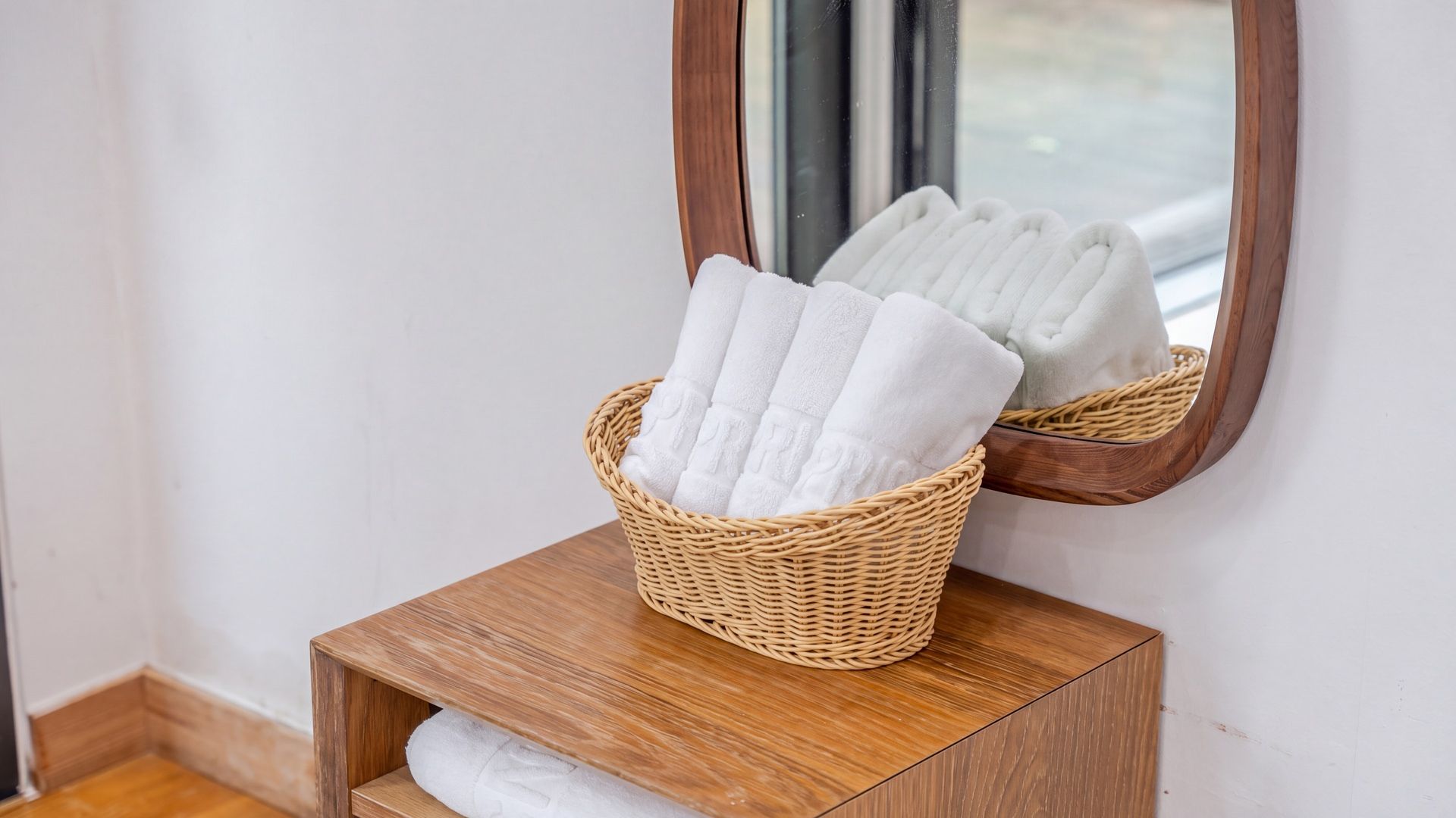 A wicker basket with folded towels on a wooden shelf next to a mirror.