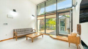 Una sala de estar moderna con un sofá, una mesa de centro y un amplio ventanal corredera que da a un espacio exterior.