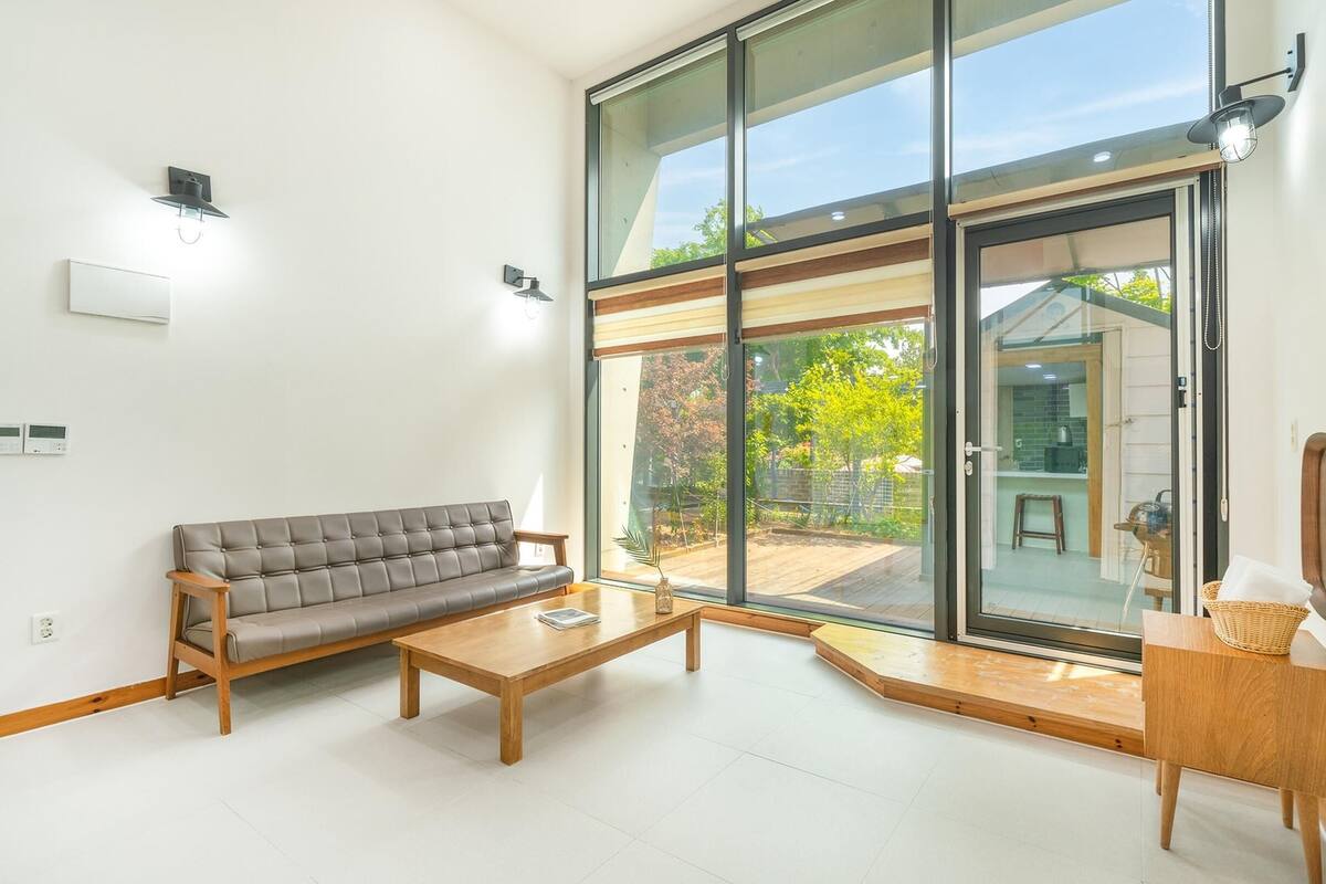 Ein modernes Wohnzimmer mit Sofa, Couchtisch und einem großen Schiebeglasfenster zum Außenbereich.