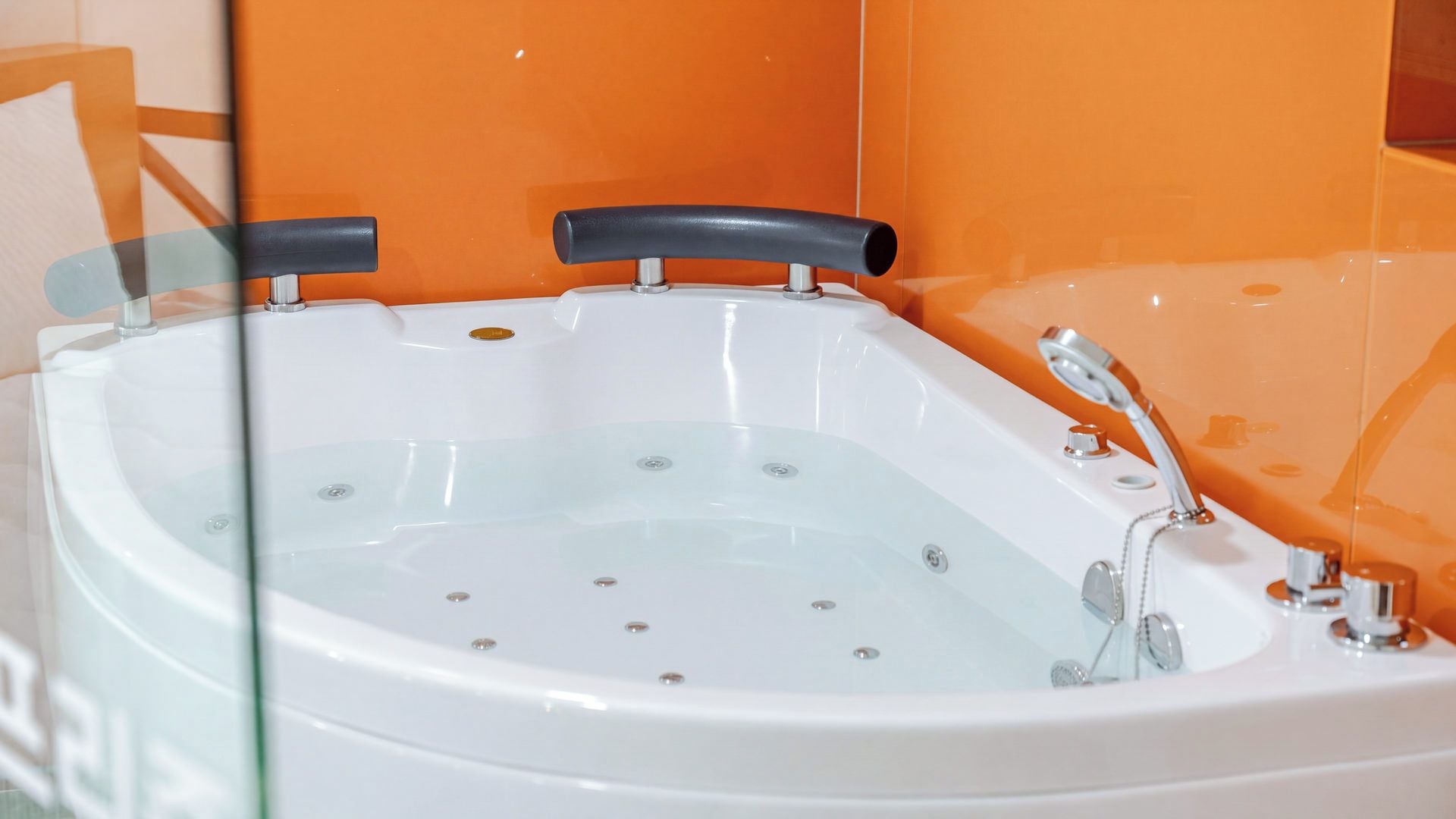 A bathtub with a faucet and a handheld showerhead, set against an orange wall.