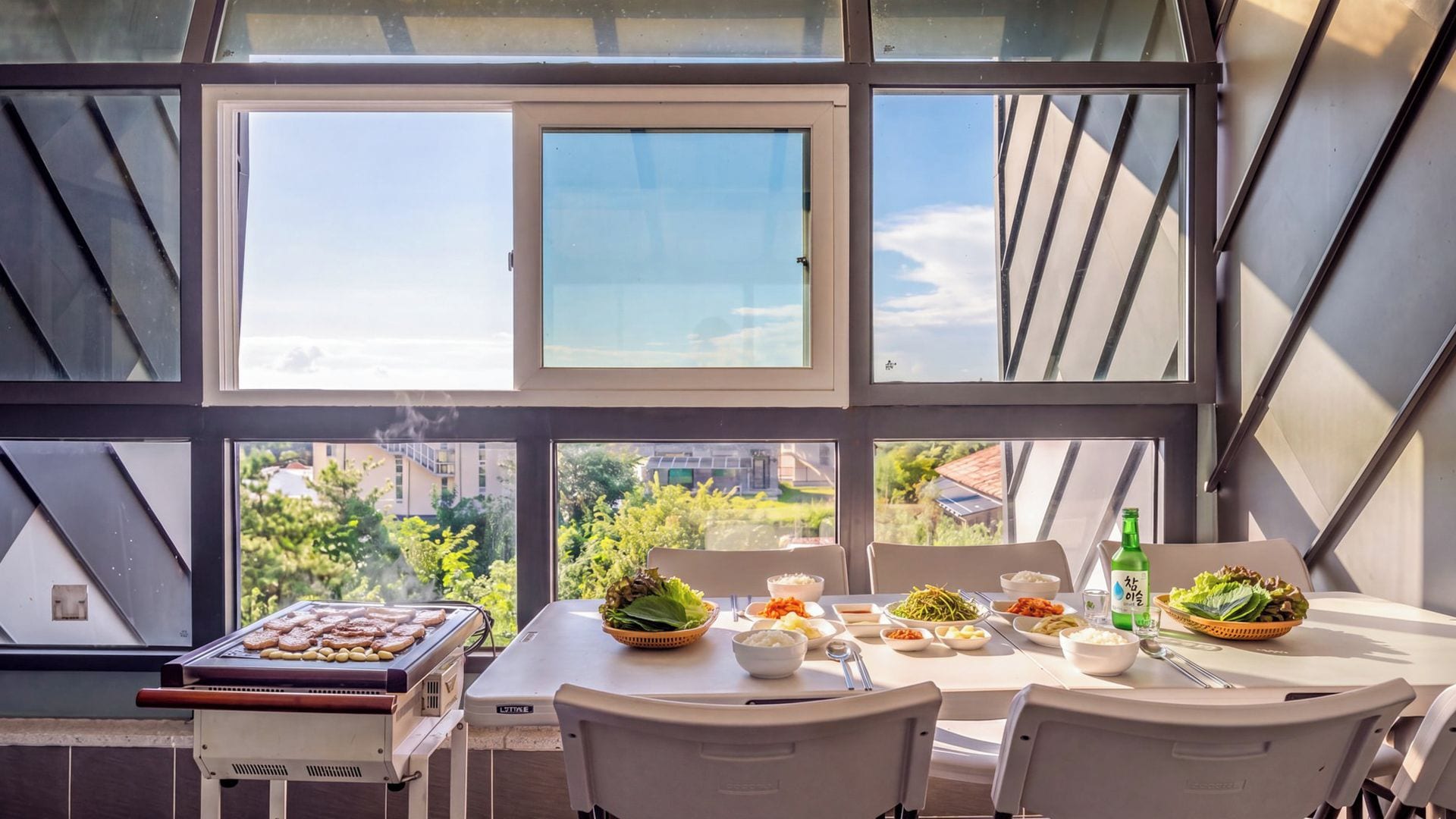 A dining area with a table set for a meal, a grill, and a view of the city through large windows.
