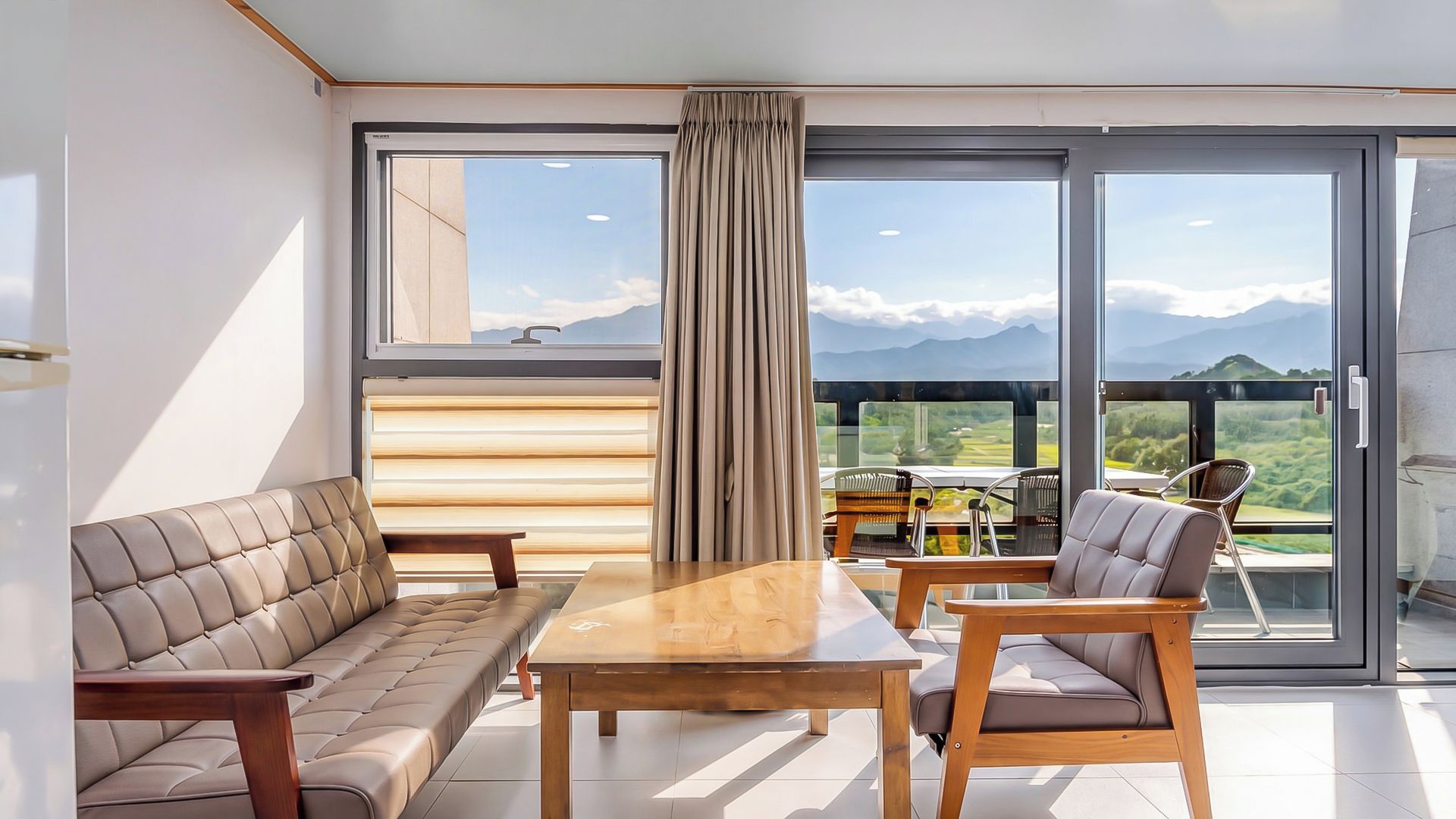 Una sala de estar moderna con sofá, sillones, una mesa y ventanas amplias con vistas a la montaña.