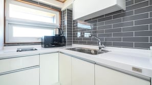 A modern kitchen with a built-in microwave, stainless steel sink, and a window with blinds. - Theprism Pension (Goseong)