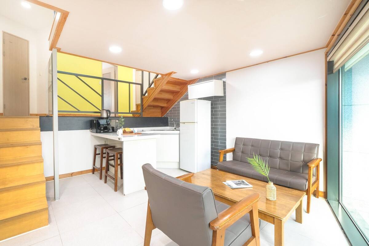 Eine moderne Küche mit Kochinsel, einer Holztreppe und einem grauen Sofa in einem hellen Wohnbereich.