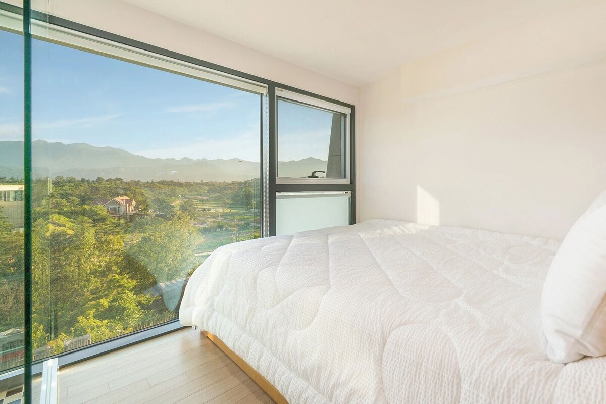 Une chambre avec une grande fenêtre, un lit et une vue sur un paysage.