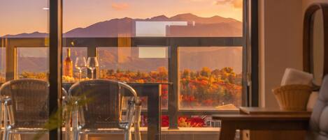 Una habitación con vistas a follaje otoñal y montañas a través de amplios ventanales.