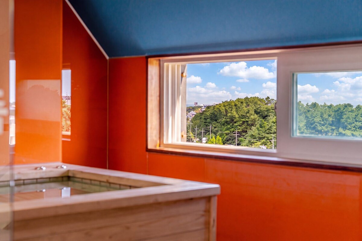 Une pièce avec une baignoire en bois, une fenêtre donnant sur une forêt et des murs orange.