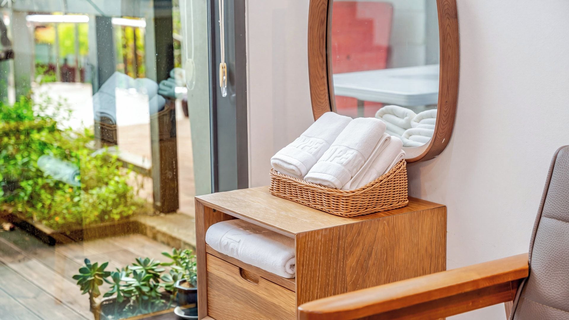 A wooden vanity with a mirror, a wicker basket holding folded towels, and a small drawer.