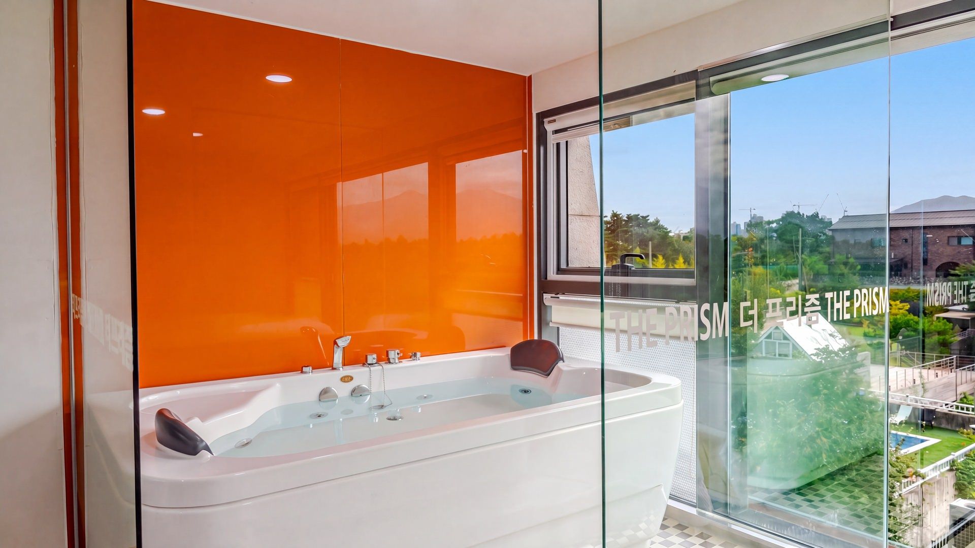 Une salle de bain moderne dotée d’une grande baignoire, d’une douche en verre et offrant une vue sur un immeuble arborant l’inscription « THE PRISM ».