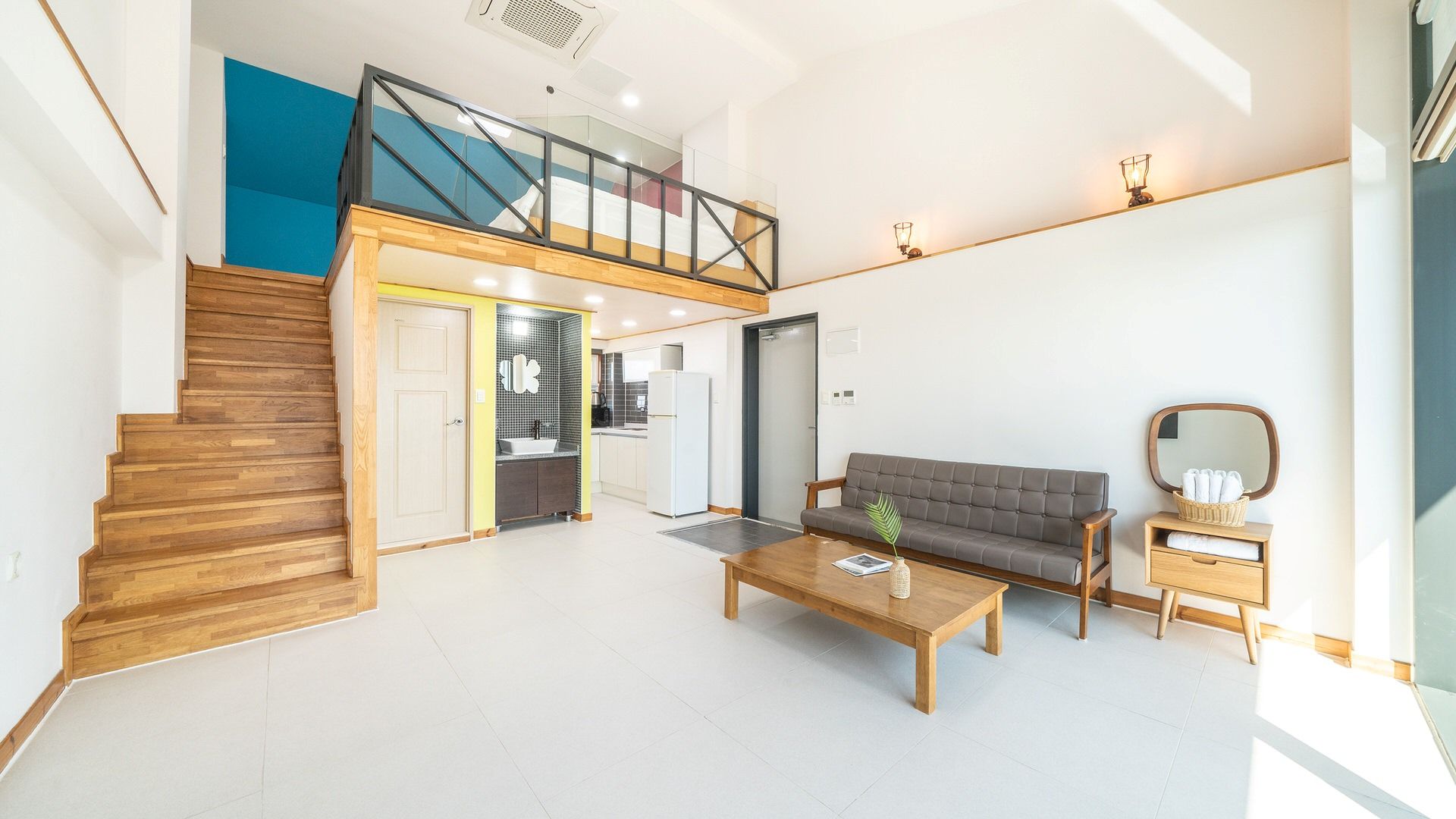 A spacious living area with a staircase, a sofa, a coffee table, and a kitchen in the background.
