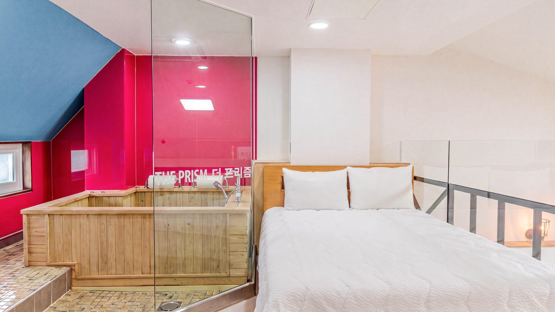 A modern hotel room with a wooden bathtub, a bed with white bedding, and a red accent wall.