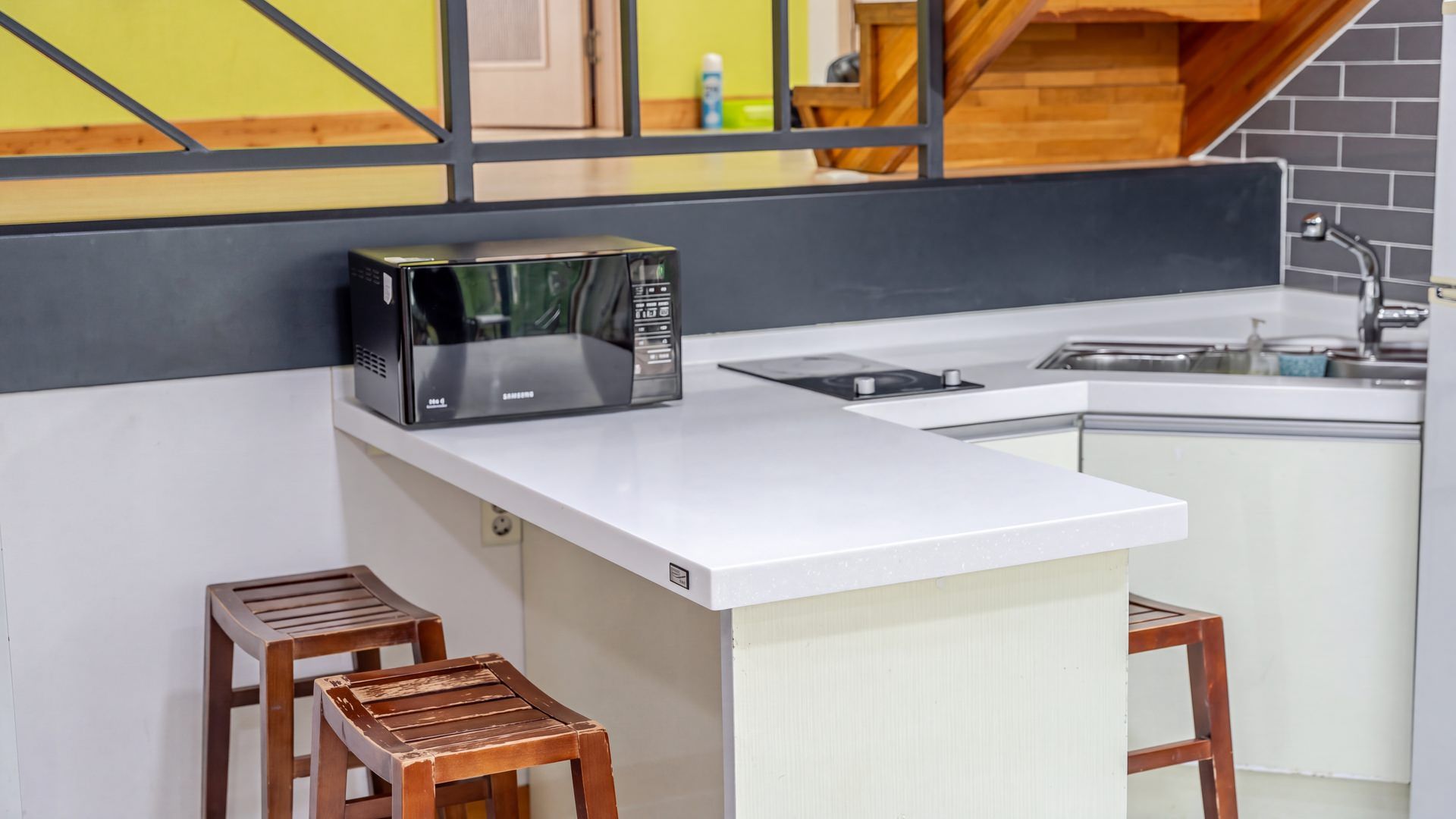 Una cocina compacta con un microondas en la encimera, un lavamanos y dos taburetes.