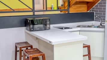 Una cocina compacta con un microondas en la encimera, un lavamanos y dos taburetes.