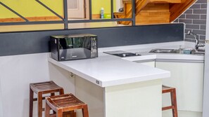 Una cocina compacta con un microondas en la encimera, un lavamanos y dos taburetes.