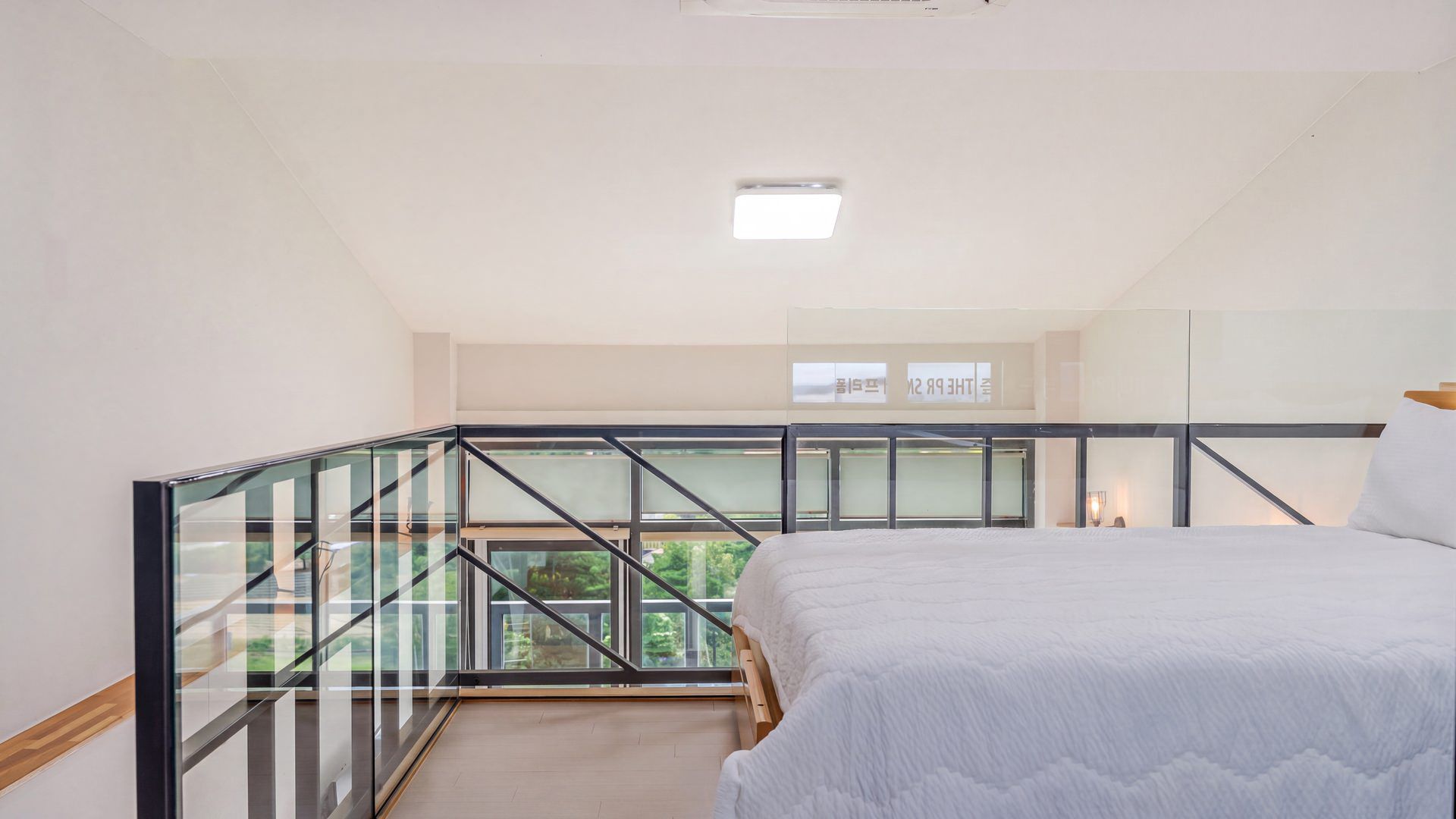 A bedroom with a large bed, a glass balcony, and a view of greenery.