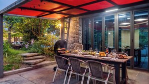Een buiten eethoek met een bakstenen pilaar, een barbecue en een gedekte tafel.