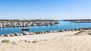 Un port de plaisance où sont amarrés de nombreux bateaux, une plage de sable et un ciel bleu azur.