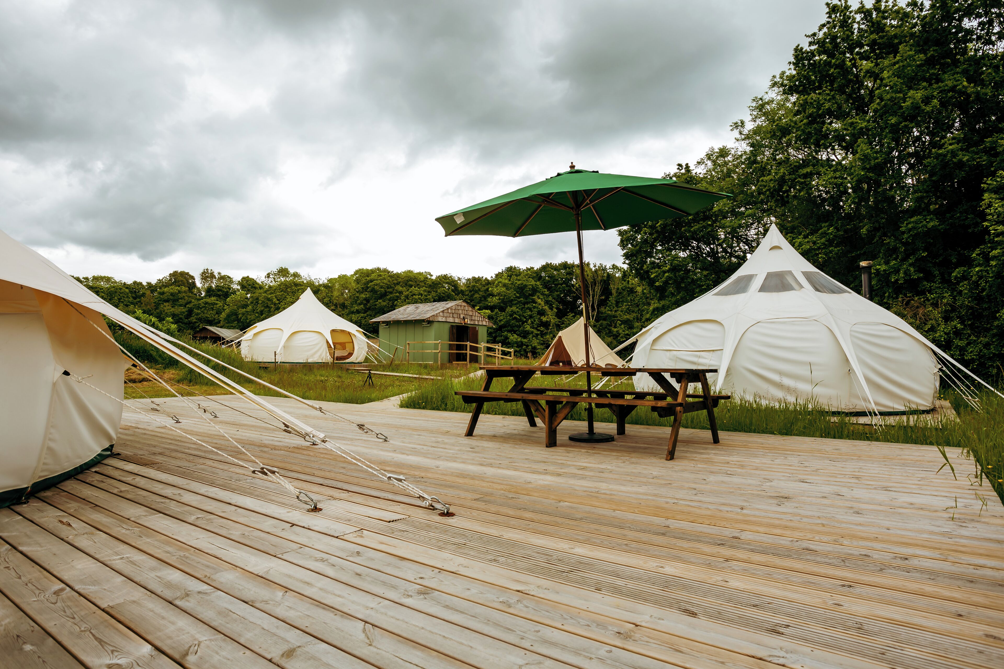 A wooden deck with white tents and a picnic table with a green umbrella.