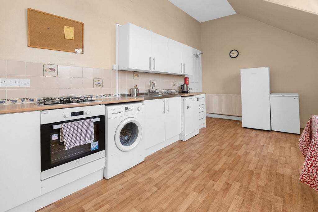 Une cuisine de taille réduite équipée d’une cuisinière à gaz, d’un four, d’un lave-linge et de meubles de rangement blancs.