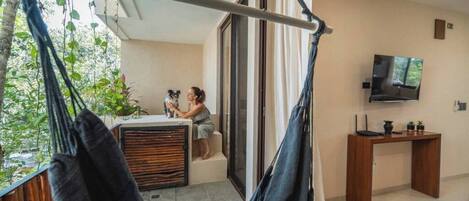 A balcony with a hammock, a person petting a dog, and a TV on a wooden stand.