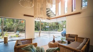 A spacious living area with wicker furniture, a staircase, and large windows offering a view of the outdoors. - Tulum Getaway+Pool+Office Area+Gym (Tulum)